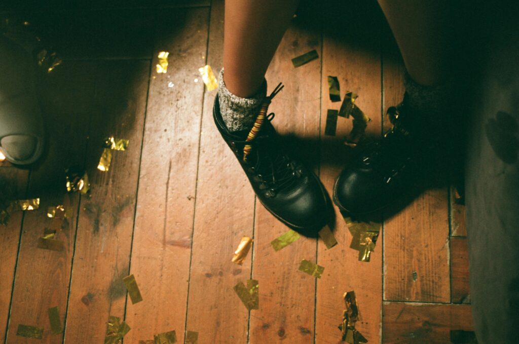Black shoes surrounded by confetti on a wooden floor, creating a festive vibe.